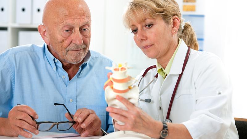 A doctor holds a model of the spine while talking to a patient.
