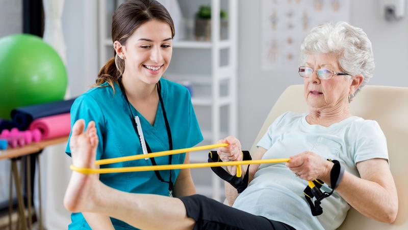 A senior woman works through a rehabilitation session with a physical therapist.