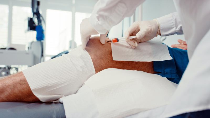 Close up photo of a doctor administering a pain injection in a patient's knee.