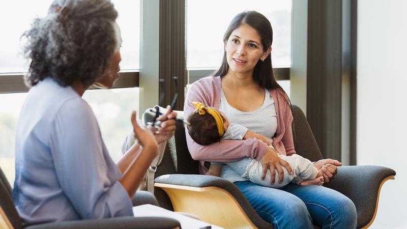 A mental health professional meets with a new mother who is holding her newborn baby.