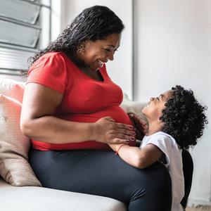 A pregnant mother looks joyfully at her small child.