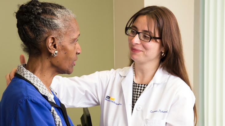 Dr Carmen Pichard examines a patient's shoulder during and office visit.