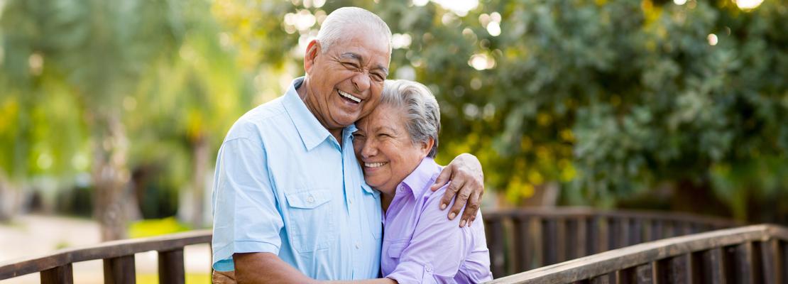 A senior couple stands together on a bridge outdoors.