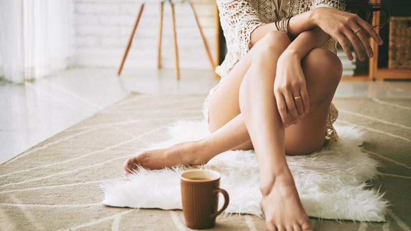 Close up photo of a woman casualysitting on the floor in her home. A coffee cup is next to her feet.