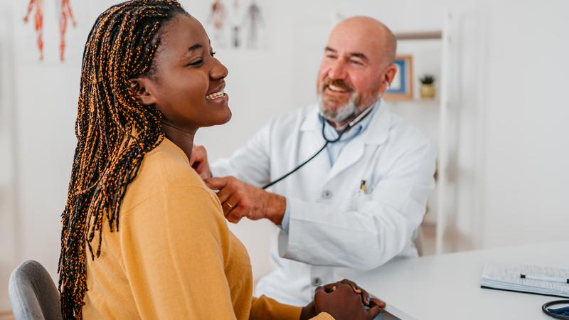 A doctor listens to a patient's heart in a clinical setting.