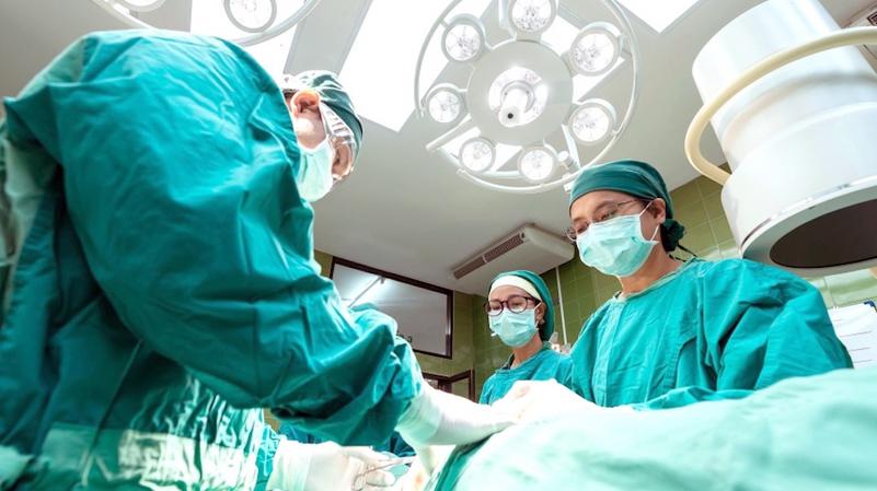 3 surgeons work on a patient in an operating room.
