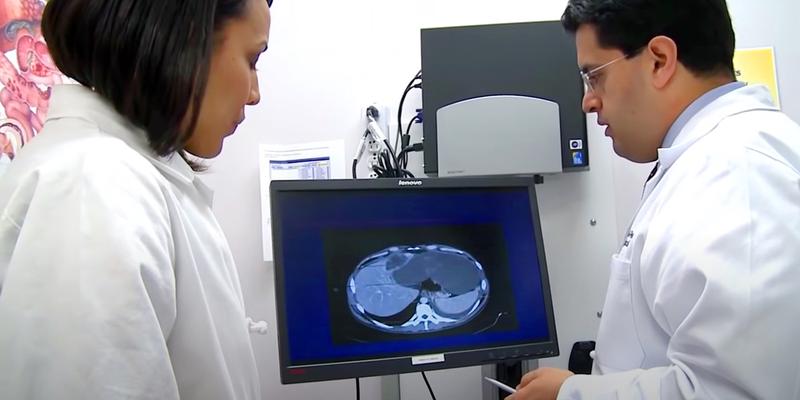 A medical assistant and Dr Waddah Al-Refaie look at an image scan of a patient's abdomen in a clinical setting.