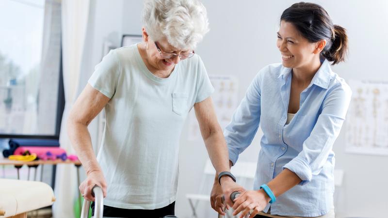 A mature adult woman uses a walker during physical therapy session with a physical therapist.