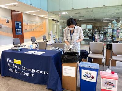 A MedStar pharmacist wearing masks works at an event to take back unused drugs and pharmaceutical paraphenalia for safe disposal.