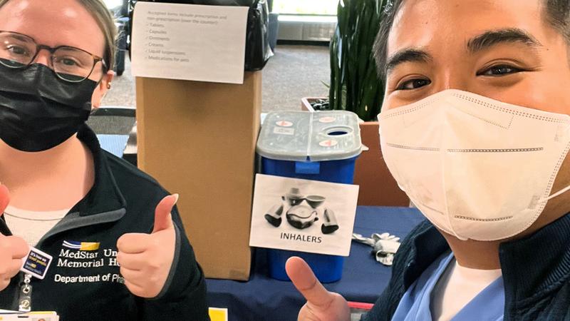 Two MedStar pharmacists wearing masks work at an event to take back unused drugs and pharmaceutical paraphenalia for safe disposal.