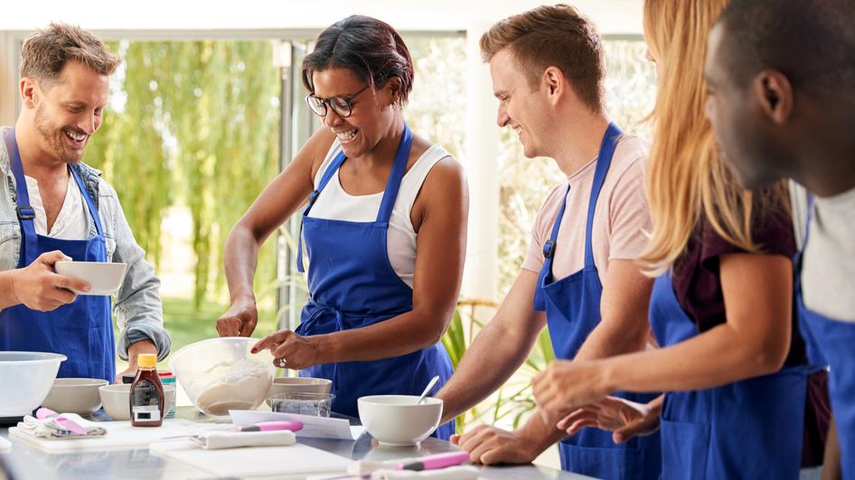 A group of adults cooks food during a cooking class.