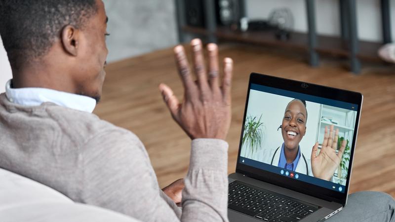 一位非裔美国男性患者在会议视频电话中与一位非洲女医生交谈。虚拟治疗师在家里的笔记本电脑上咨询在线预约的年轻人。远程医疗聊天，远程医疗会议
