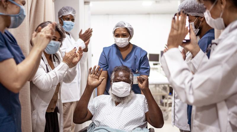 A team of physicians stands in a hallway and claps for a patient who is being discharged from the hospital.