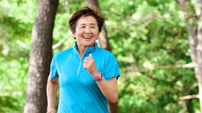A senior woman enjoys a run in the woods on a summer day.