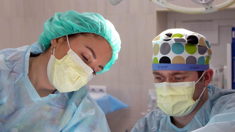 Close up photo of 2 surgeons, wearing masks, in an operating room.