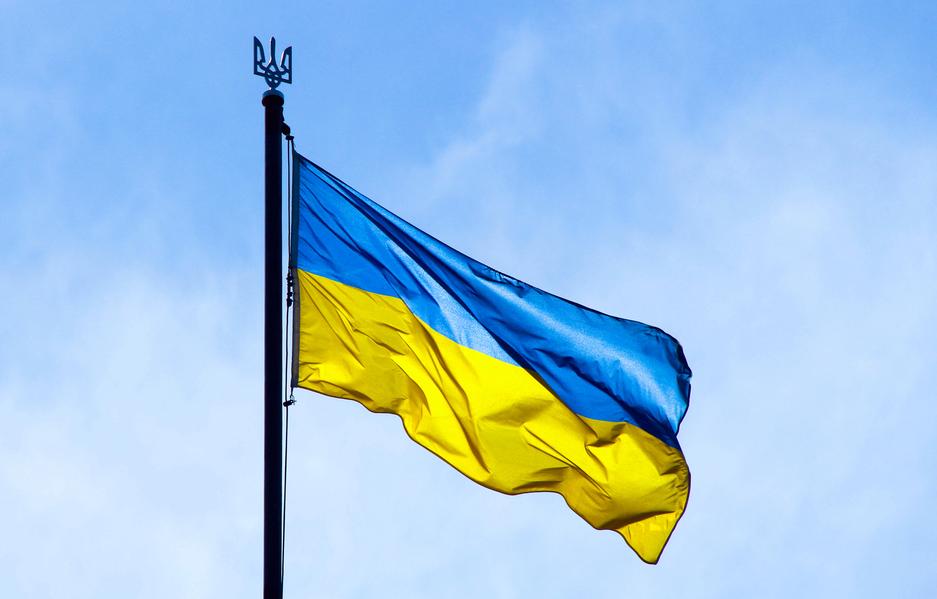 Ukrainian flag is pictured in the rays of the rising sun on a background of sky. Bicolor blue and yellow national flag of Ukraine on a flagpole and coat of arms of Ukraine trident. Official symbol of Ukraine.