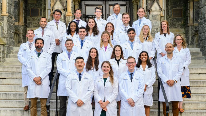 The current class of urology residents at MedStar Georgetown University Hospital stands together on the steps of a historic stone building and pose for a class photo.