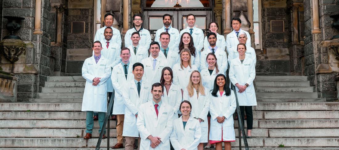 The current class of urology residents at MedStar Georgetown University Hospital stands together on the steps of a historic stone building and pose for a class photo.