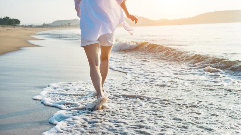 A woman walks in the waves on a beach at sunrise.