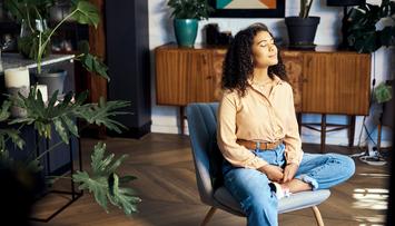 A woman closes her eyes while she sits in a chair in a peaceful office.