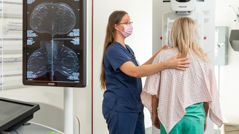 A radiology technician positions a woman for a mammogram scan in a clinical setting.