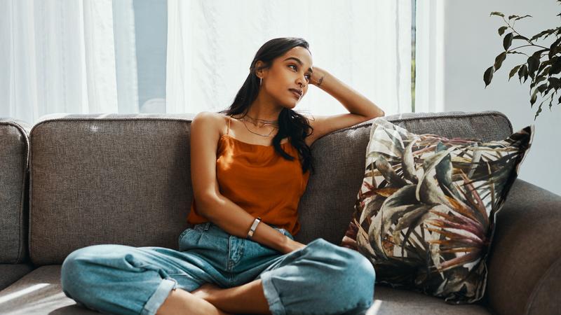 A young woman looking thoughtful while relaxing on the sofa at home
