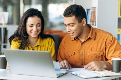 Two young adults study using a laptop computer in a library.